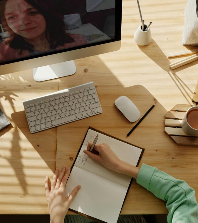 A student taking notes during a video call for online learning at home.